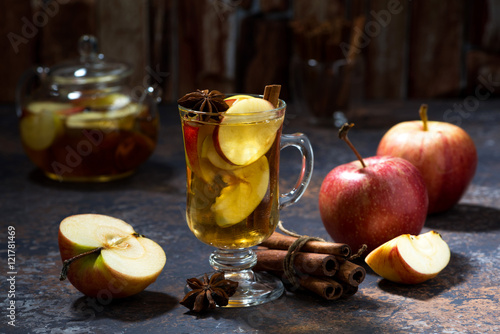 glass of hot apple tea with spices on dark table