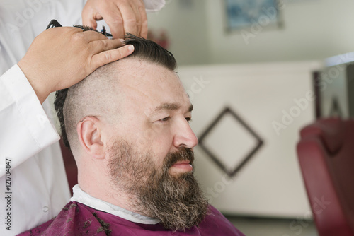 Barber makes a mohawk hairstyle of a adult bearded man