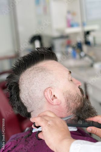Male barber cuts the beard of a adult man with a mohawk