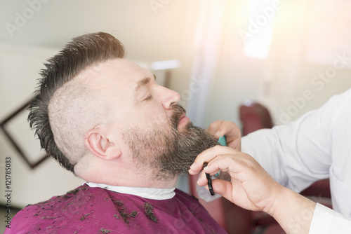 Male barber cuts the beard of a adult man with a mohawk photo