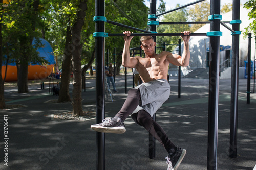 Young man doing pull ups on horizontal bar outdoors, workout, sp