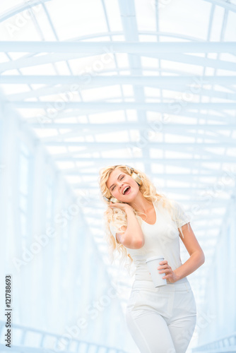 Morning rhythm / Beautiful young woman with music headphones, standing on the bridge with a take away coffee cup and posing against urban background. © Fisher Photostudio
