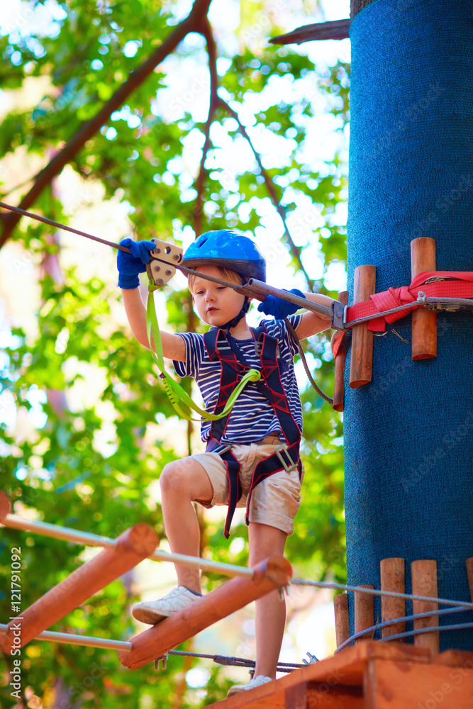 Fototapeta premium young boy passing the cable route high among trees, extreme sport in adventure park