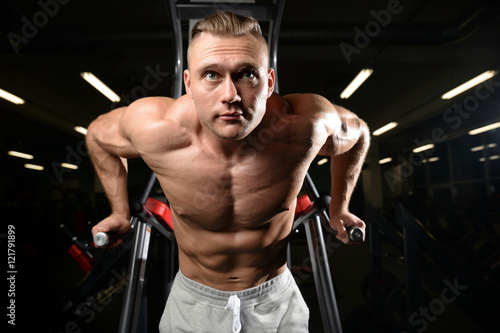 Handsome muscular bodybuilder man doing exercises in gym.