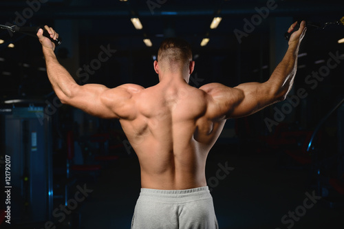 Handsome muscular bodybuilder man doing exercises in gym.