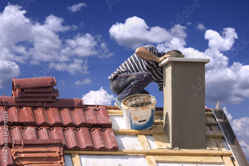 Obraz na plátně Roofer builder worker repairing a chimney stack on a roof house