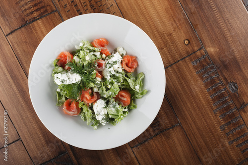 Salad with salmon fish and cream cheese in a white plate. Wooden background