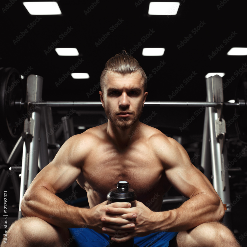 Young muscular man sitting with a bottle of water in the gym Young muscular man sitting with a bottle of water in the gym