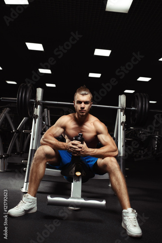 Young muscular man sitting with a bottle of water in the gym