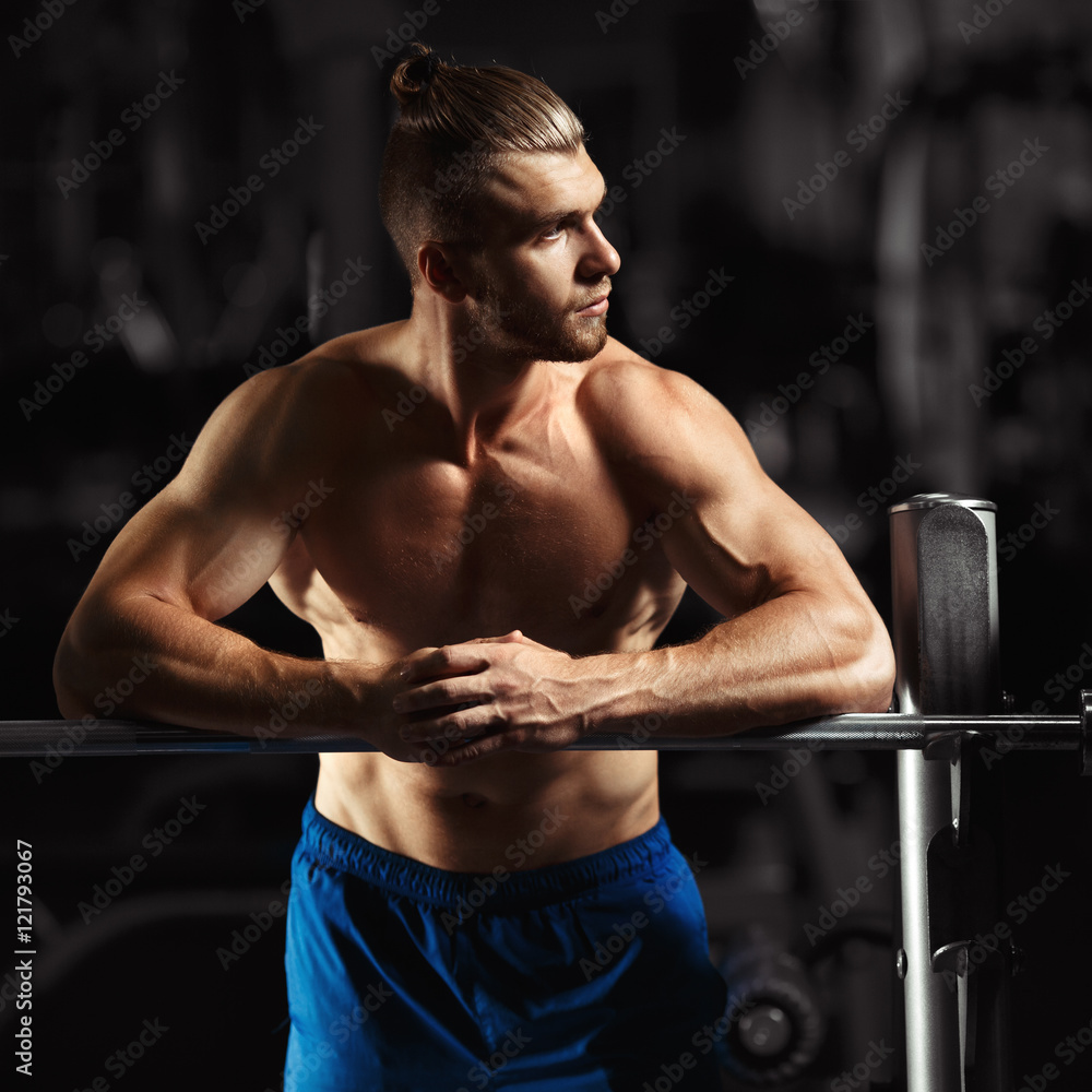 Fototapeta premium Attractive muscular bodybuilder guy prepare to do exercises with barbell in a gym