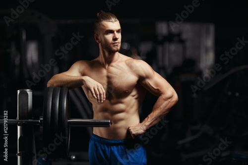 Attractive muscular bodybuilder guy prepare to do exercises with barbell in a gym