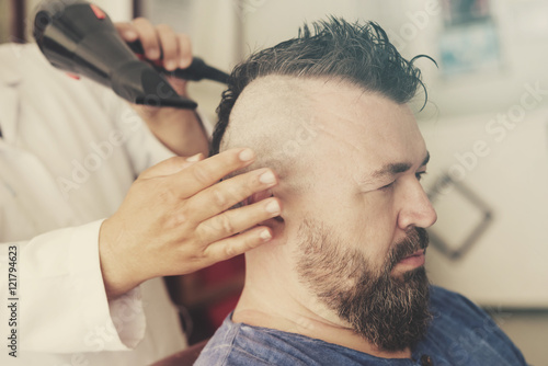 Male barber dry head using a hair dryer of a adult man with a mohawk