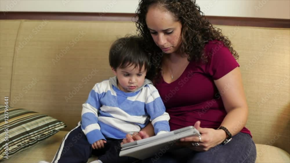 A pretty Hispanic mother peaks her toddlers attention with something on an electronic tablet she is using to educate and entertain him. A pretty Hispanic mother peaks her toddlers attention with something on an electronic tablet she is using to educate and entertain him.