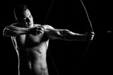 Shirtless guy aiming with a bow and arrow