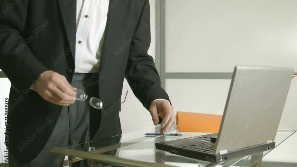 A businessman stands next to desk typing with one hand on his laptop computer as if about to leave the scene. Canon C300 A businessman stands next to desk typing with one hand on his laptop computer as if about to leave the scene. Canon C300