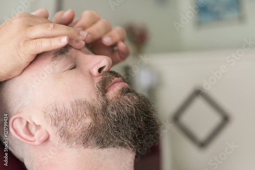 Male barber doing massage for the face of a adult bearded man with a mohawk