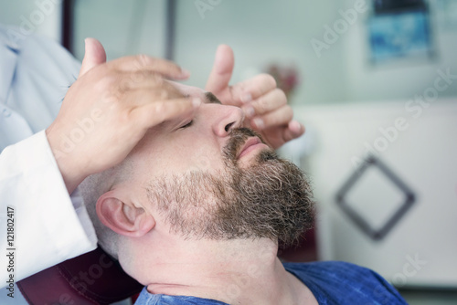 Male barber doing massage for the face of a adult bearded man with a mohawk. Toned