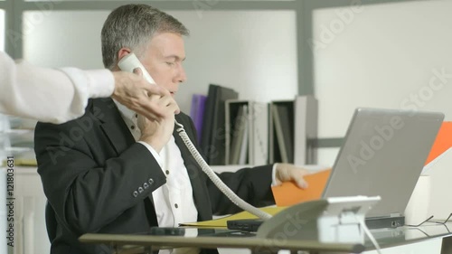 A man on his office desk phone gets no consideration from a coworker who needs her paperwork.  Canon C300 photo