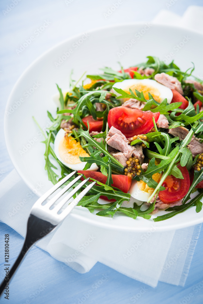 Fresh salad with tuna, tomatoes, eggs, arugula and mustard on blue wooden background close up. Healthy food. Fresh salad with tuna, tomatoes, eggs, arugula and mustard on blue wooden background close up. Healthy food.
