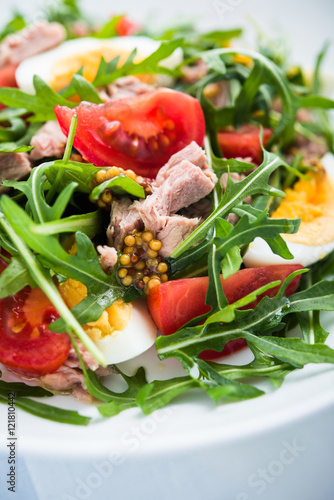 Fresh salad with tuna  tomatoes  eggs  arugula and mustard on blue wooden background close up. Healthy food.
