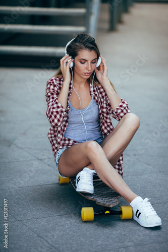 young adult woman sitting on longboard and wearing headphones