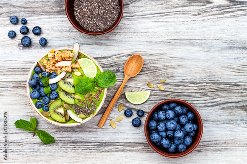 Schilderij op canvas Matcha green tea breakfast superfoods smoothies bowl topped with chia, flax and pumpkin seeds, bee pollen, granola, coconut flakes, kiwi and blueberries
