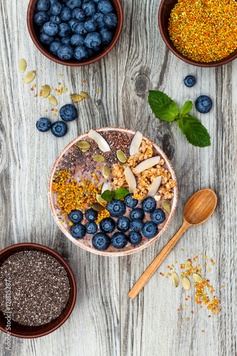 Acai breakfast superfoods smoothies bowl topped with chia, flax and pumpkin seeds, bee pollen, granola, coconut flakes and blueberries. Overhead, top view, flat lay