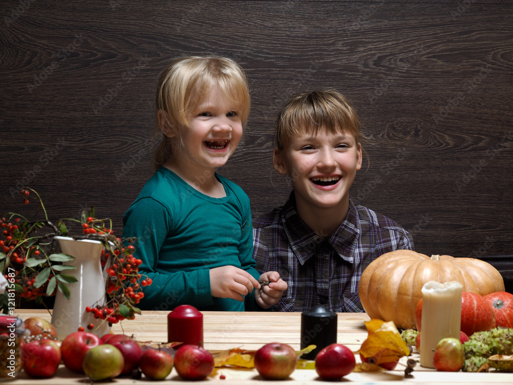 Naklejka premium Children are prepared to meet the autumn holiday Halloween. Two sisters at the table. Pumpkin, rowan tree, decorations for the holiday. Laughter, joy, emotion,