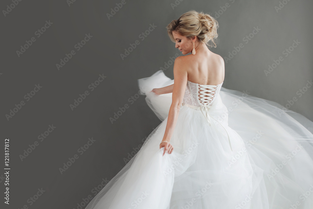 Dancing young bride in luxurious wedding dress. Pretty girl in white. Emotions of happiness, laughter and smile, gray background Dancing young bride in luxurious wedding dress. Pretty girl in white. Emotions of happiness, laughter and smile, gray background