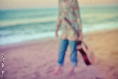 Unfocused photo of elegant woman walking on the beach with guitar, outdoor background