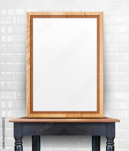 Blank wooden photo frame leaning at white tile wall on black vin