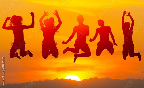 Teenage boys and girls jumping high in the air against colorful sunset sky in summer