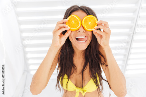 Woman in bikini holding two halves of orange against eyes