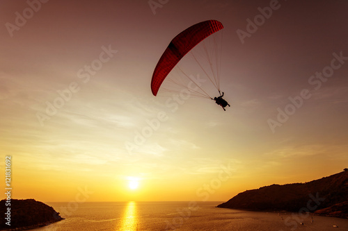 Silhouette of skydiver flies on background sunset sky and sea