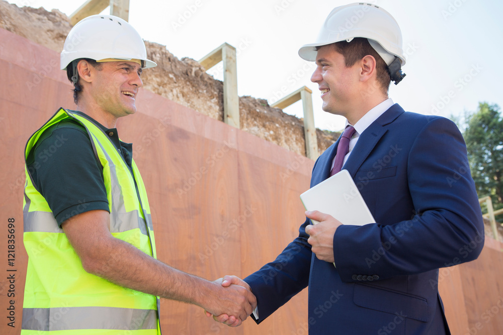 Businessman Shaking Hands With Builder On Construction Site Businessman Shaking Hands With Builder On Construction Site