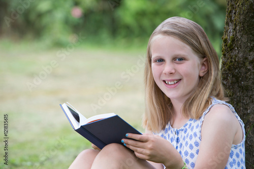 Girl Sitting Against Tree In Garden Reading Book © Daisy Daisy