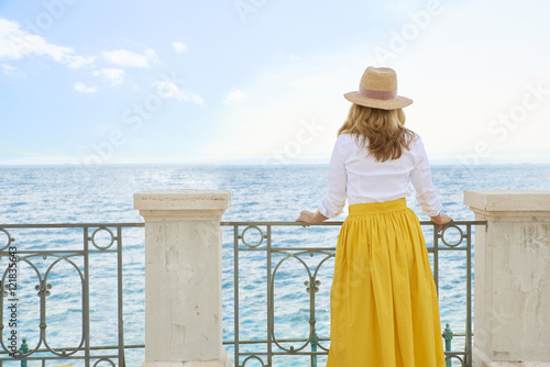 Woman by the sea. Full length shot of an elegant middle aged lady standing at balcony by the ocean and enjoying the view. © sepy