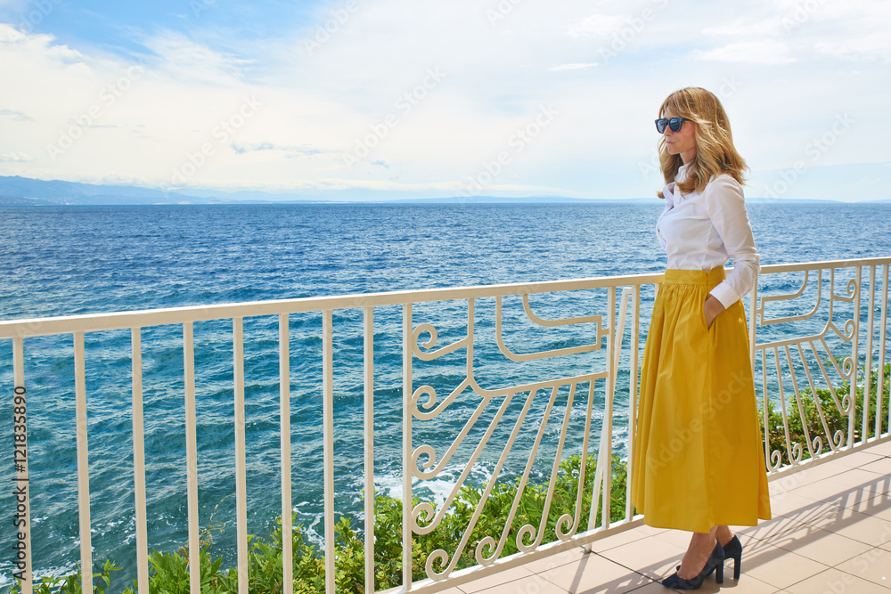 Woman by the sea. Full length shot of an elegant middle aged lady standing at balcony by the ocean and enjoying the view.