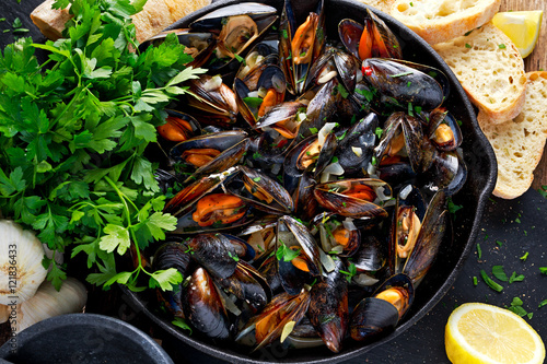 Boiled mussels in iron pan cooking dish. with herbs, butter, lime, parsley, garlic and fresh bread. photo