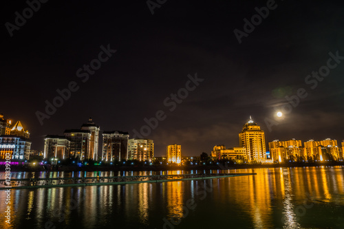 Astana  Kazakhstan. Ishim river embankment in the moon night with buildings and reflection in the water