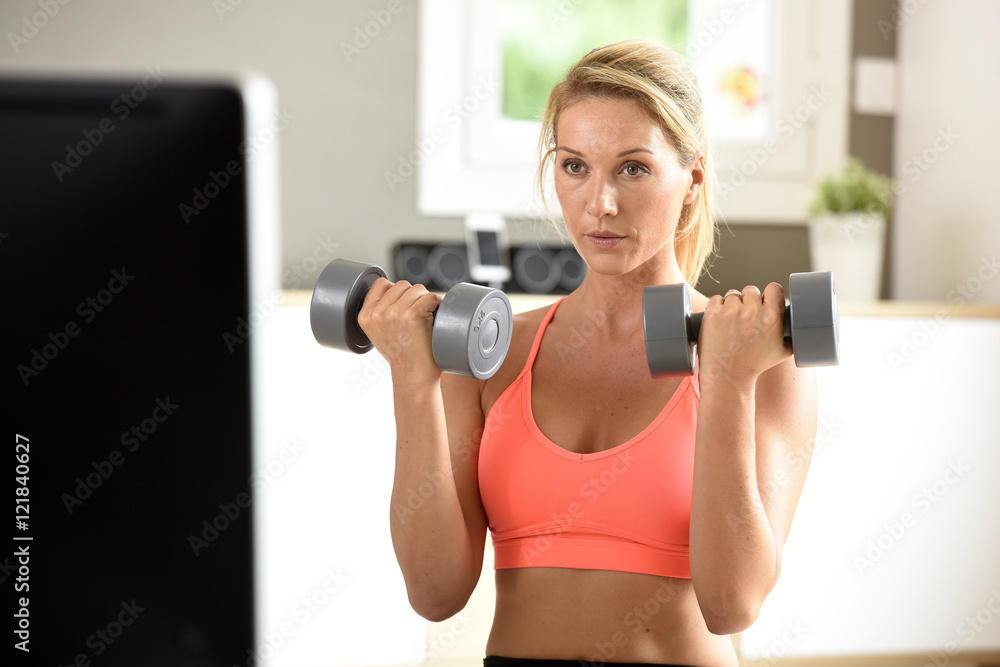 Fitness girl lifting dumbbells in front of TV program