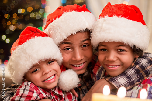 Three kids in Christmas hats. Smiling afro boys on Christmas. Three happy brothers on holidays. Christmas evening at family house.