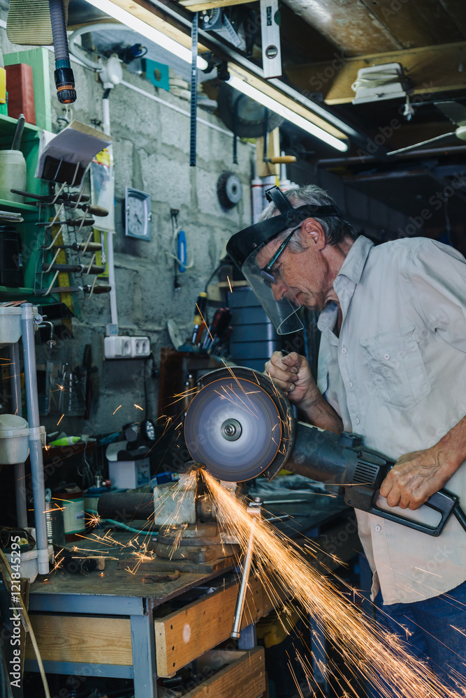 Side view of senior workman working with circular grinder in his hands producing flash of sparkles Side view of senior workman working with circular grinder in his hands producing flash of sparkles