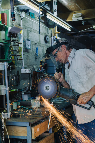 Side view of senior workman working with circular grinder in his hands producing flash of sparkles