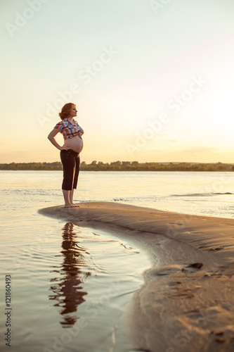 Pregnant red haired woman is standing on the river background. © diter