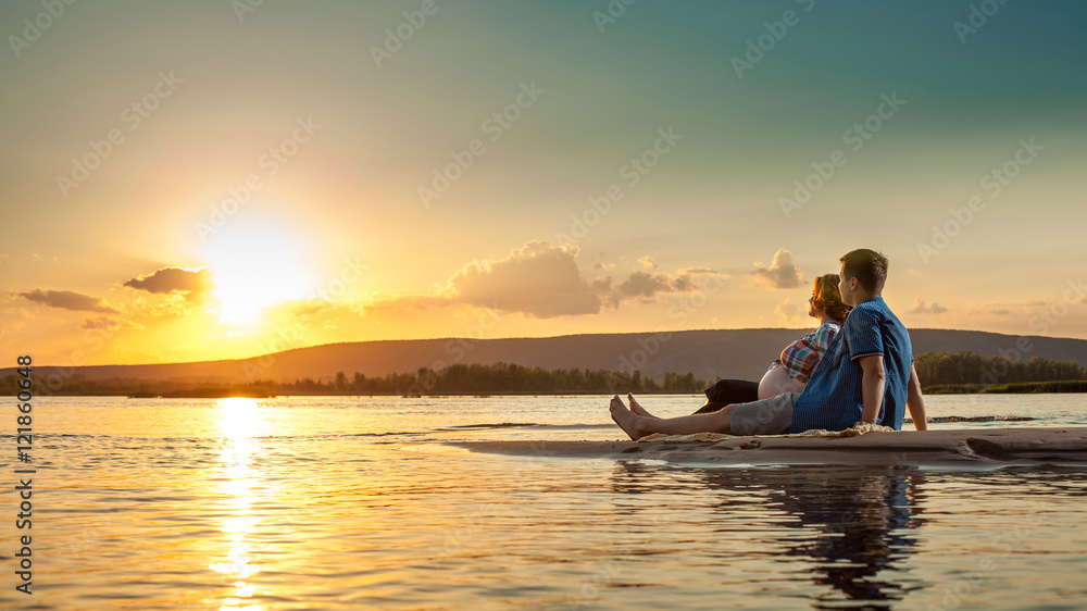 Beautiful couple is sitting on the beach and looking at the suns Beautiful couple is sitting on the beach and looking at the suns