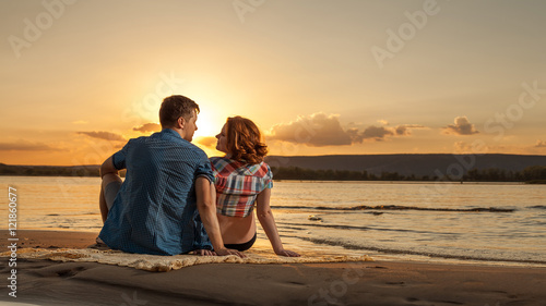 Beautiful couple is sitting on the beach and looking at each oth