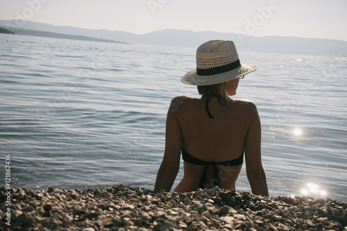 Young beautiful girl in black bathing suit with straw hat relaxing on the beach photo