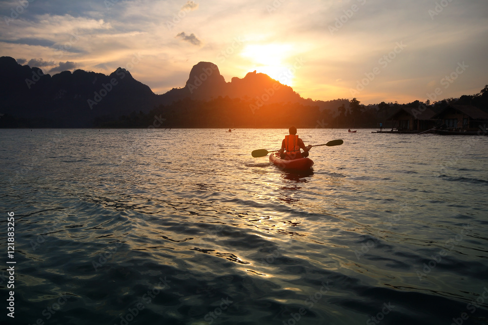 Obraz premium Silhouette scenery during sunset with a man paddling the kayak at natural attractions in Ratchaprapha Dam,Khao Sok National Park,SuratThani Province in Thailand. Traveling and recreation Concept.