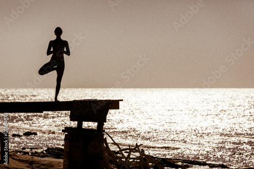 Foto Yoga on a dock with the ocean in the background at sunset in silhouette